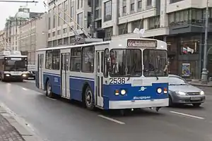 Aquamarine-and-white trolleybus under a viaduct