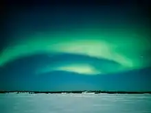 Curtains of greenish light in the night sky over a flat, snowy landscape