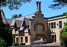 Partial view of a Gothic Revival sandstone mansion with crow-stepped gables and pairs of tall chimneys