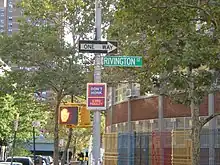 A metal pole is looked head on, with a green rectangular sign saying "Rivington St" in all capital letters and the "St" in superscript, and a black sign with a white arrow and the all-capital "One Way" within the arrow immediately above the green sign.