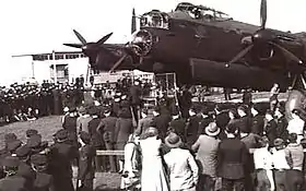 Crowd of uniformed and civilian personnel in front of four-engined military monoplane