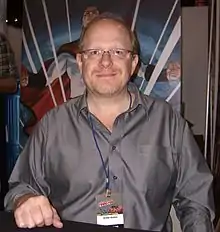 Waid looking toward the camera and smiling in front of an Irredeemable poster