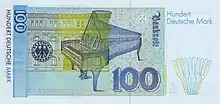 Banknote in light blue with yellowish green and beige, focused on an open grand piano, with a building in the left background