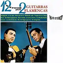 Two men in black suits playing flamenco guitars in front of a blue background