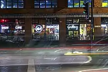 A view of the front of a building with large windows and neon signs with light streams from a long exposure shot.