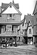 Image of the front of the house whilst at 16 Edumund Street, with a horse and carriage outside, and one man and three women posed outside, and a sign which reads W May Boot and Shoe Maker.