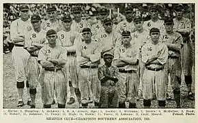 A black and white photograph of seventeen standing on a baseball field wearing light baseball uniforms with dark stripes and caps.