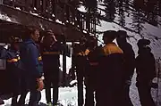 Skiers standing on snow near a balcony.