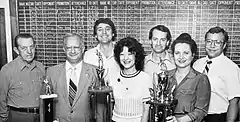 Five men and two women pose with three trophies.