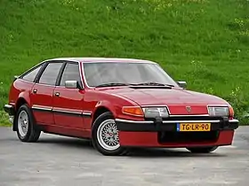 Full view from front right corner aspect of a red sporting saloon car with alloy wheels, a rear spoiler and a front air dam against a grassy bank to rear