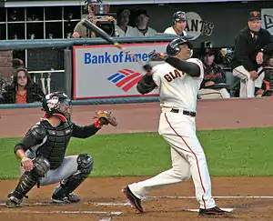 An African-American man in a white baseball uniform with "GIANTS" on the chest takes a left-handed baseball swing as a catcher kneels behind him to receive the pitch.