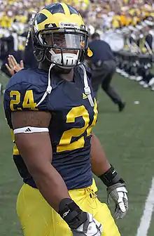 African American male in football uniform standing on a football field with his helmet on.