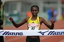 A woman begins to celebrate at the finish line of a road race.