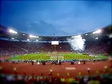 A panoramic view of a stadium. Several people are on the pitch.