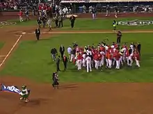 A group of men in red and white baseball uniforms gather on a baseball field.