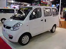  Front-three-quarter view of a small passenger van with door mirrors, flush headlights, front fog lamps, body-coloured bumpers, rear-sliding door, and hubcaps that has "420,600.-" written on the windscreen