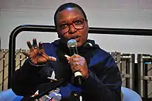 Meshell Ndegeocello speaking holding a mic in her left hand.