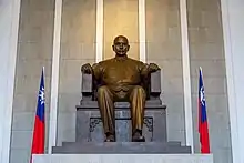 Bronze statue of man on stone chair with a Taiwan flag on either side