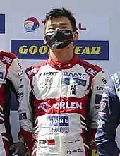 Photograph of Ye Yifei wearing a white uniform with red trim and a black medical mask on his face