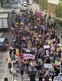 Students walking through a street with signs and banners protesting cuts.