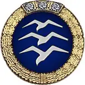 Badge: on a blue disc, silhouette of three white birds stacked in flight, the whole surrounded by a gold wreath surmounted with three diamonds