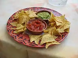 A bowl of tortilla chips with red salsa and green guacamole