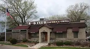 A one-story stone building with burgundy awnings and a sign announcing 5-8 Club Tavern & Grill