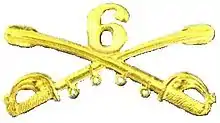 A computer generated reproduction of the insignia of the Union Army 6th Regiment cavalry branch. The insignia is displayed in gold and consists of two sheafed swords crossing over each other at a 45-degree angle, pointing upwards with a Roman numeral 6