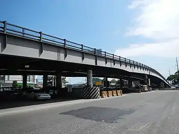 Steel poles 164–166 (of anchor or flag design) along Jose Abad Santos Avenue, San Fernando, Pampanga. The square asphalt marking at the middle of the road is the location where steel pole 167 was originally located before its relocation at the side of an avenue in 2011 using NAPOCOR-era steel pole 275 and also retiring pole 167 itself.