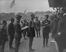 A black-and-white photograph of a man surrounded by military people and receiving a medal from an older military man