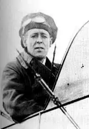 Half-portrait of man in cap and goggles seated in the open cockpit of a biplane