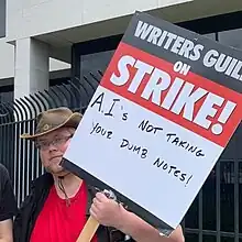 A picketer is carrying a sign deriding film studios' proposals to replace writers with generative AI.