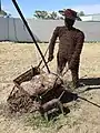 Artwork made from barbwire, of a person pushing a wheelbarrow, with a dog (2021).