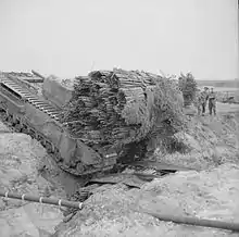 A Churchill tank, carrying a fascine, crosses a ditch using an already deployed fascine, 1943.