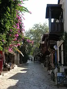 A street in Kaş with traditional houses and a Lycian tomb in the background