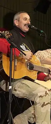 Country music singer Aaron Tippin, seated and strumming a guitar while singing into a microphone