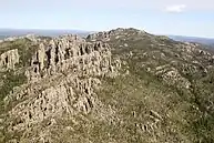 An aerial view of a rocky hillside partly covered by green and yellow vegetation.