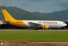 An aircraft painted in white colour with the name Air Hong Kong painted in red on the fuselage, and in yellow colour from the rear to the tail with the name DHL painted in red on the tailfin.