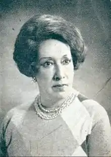 Portrait of a woman with short hair gazing left and wearing pearled earrings and necklace over a argyle-patterned blouse.