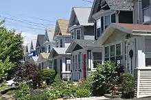 A row of detached wooden gabled houses on the right, all following a similar basic plan but of different colors, with small lawsn in front