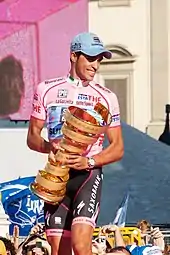 A man wearing a pink jersey and black shorts while holding a golden trophy.