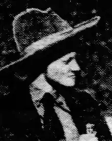 A young white woman dressed in a man's wide-brim hat, necktie, shirt, and jacket, photographed in profile