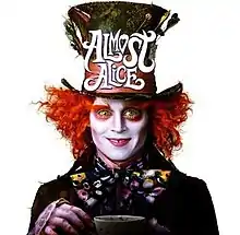 The mad hatter staring directly at the viewer holding up a cup of tea.