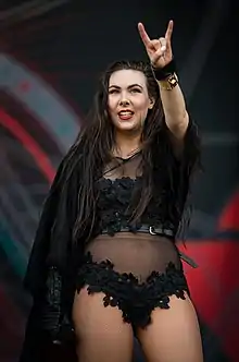 Elize Ryd in black clothes raising her left hand making the sign of the horns