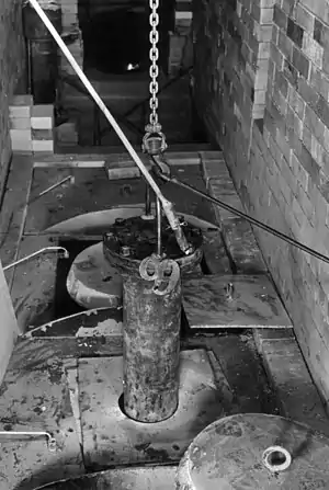 A "bomb" (pressure vessel) containing uranium halide and sacrificial metal, probably magnesium, being lowered into a furnace