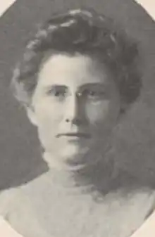 A white woman wearing glasses and a high-collared shirtwaist, her hair in a bouffant updo