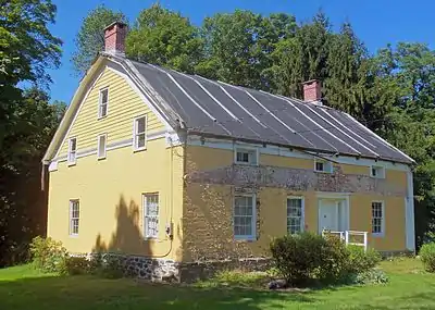 A yellow house with a painted brick front and wooden clapboard sides. It has a peaked roof with brick chimneys at either end.