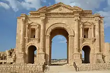 Looking North, a large stone arch can be seen, bathed by the light of the sun on the golden stone. It has many decorative features, and a smaller arch on each side of the central one.