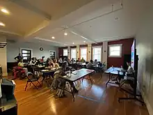 many participants seated at tables watch a presentation in a sunlit room