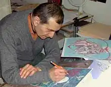 Katz bent over an art board, drawing